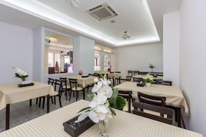 Un restaurant doté de nombreuses tables et chaises, chacune recouverte d’une nappe à carreaux. Des plantes en pot sont disposées sur les tables, et la salle présente un design moderne avec des murs blancs et des luminaires au plafond.