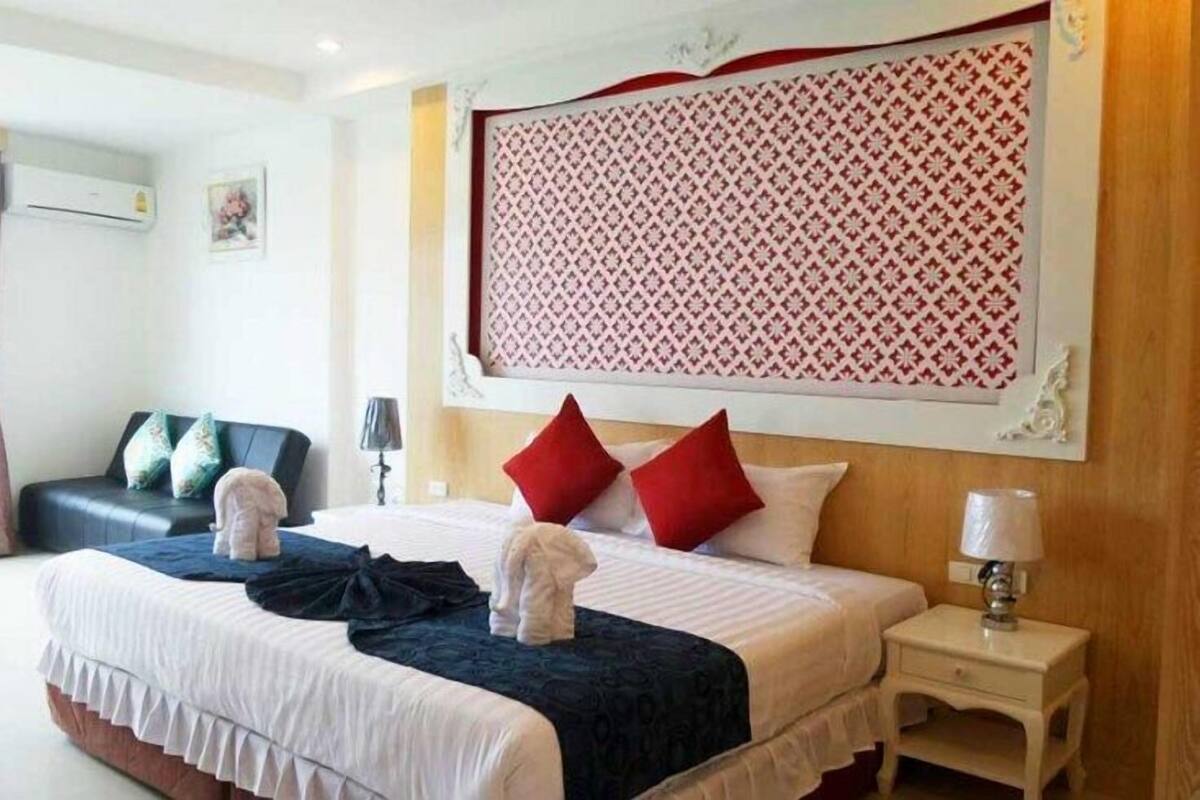 A hotel room with a bed, a nightstand, a lamp, a window with curtains, and a wall-mounted decorative panel.