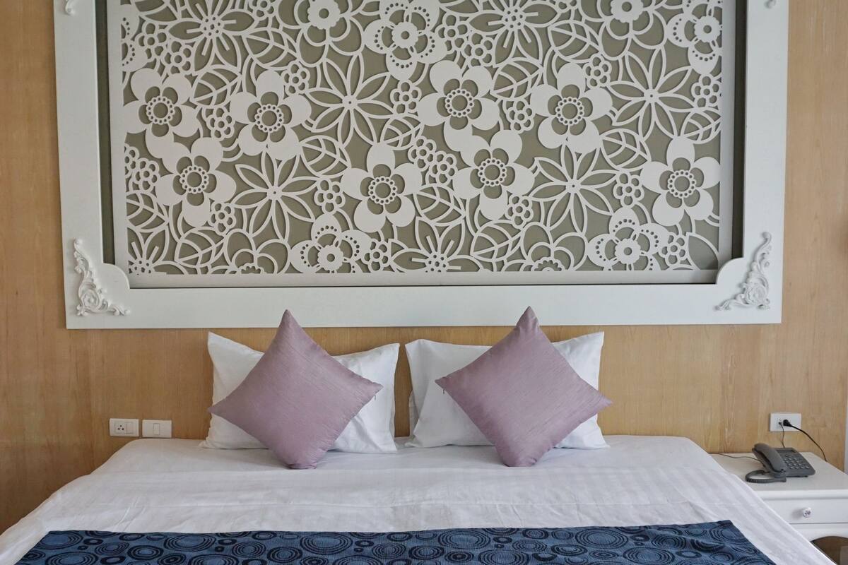 A neatly made bed with a blue patterned bedspread, two pillows, and a decorative wall panel above.