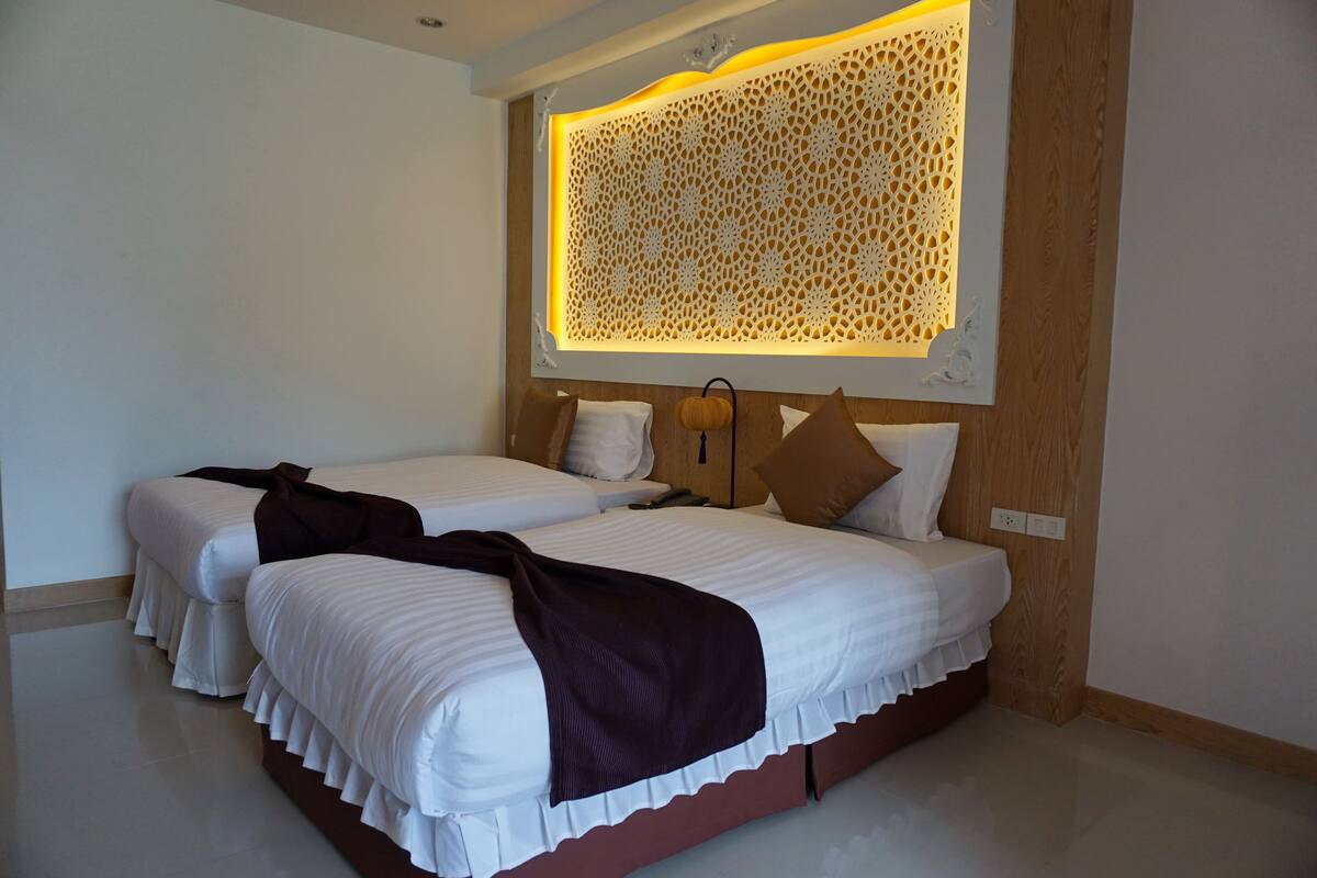 A hotel room with two beds, a decorative wall panel, and a bedside table with a lamp.