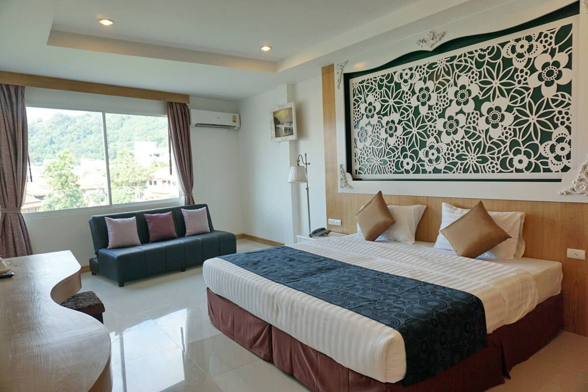 A hotel room with a large bed, a sofa, a dining table, and a view of the outdoors.