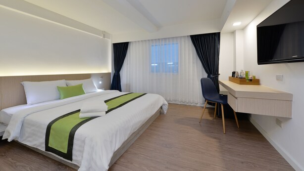 A modern hotel room with a neatly made bed, a desk with a chair, a flat-screen TV mounted on the wall, and a large window with curtains. - iCheck inn Sukhumvit 19 (Bangkok)