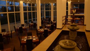 A restaurant with multiple dining tables and chairs, large windows, and a fountain. - Sole Luna Resort & Spa (Tangalle)
