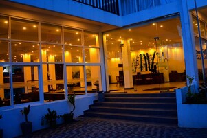 Um hall de hotel moderno com janelas amplas, uma escadaria e plantas em vasos.