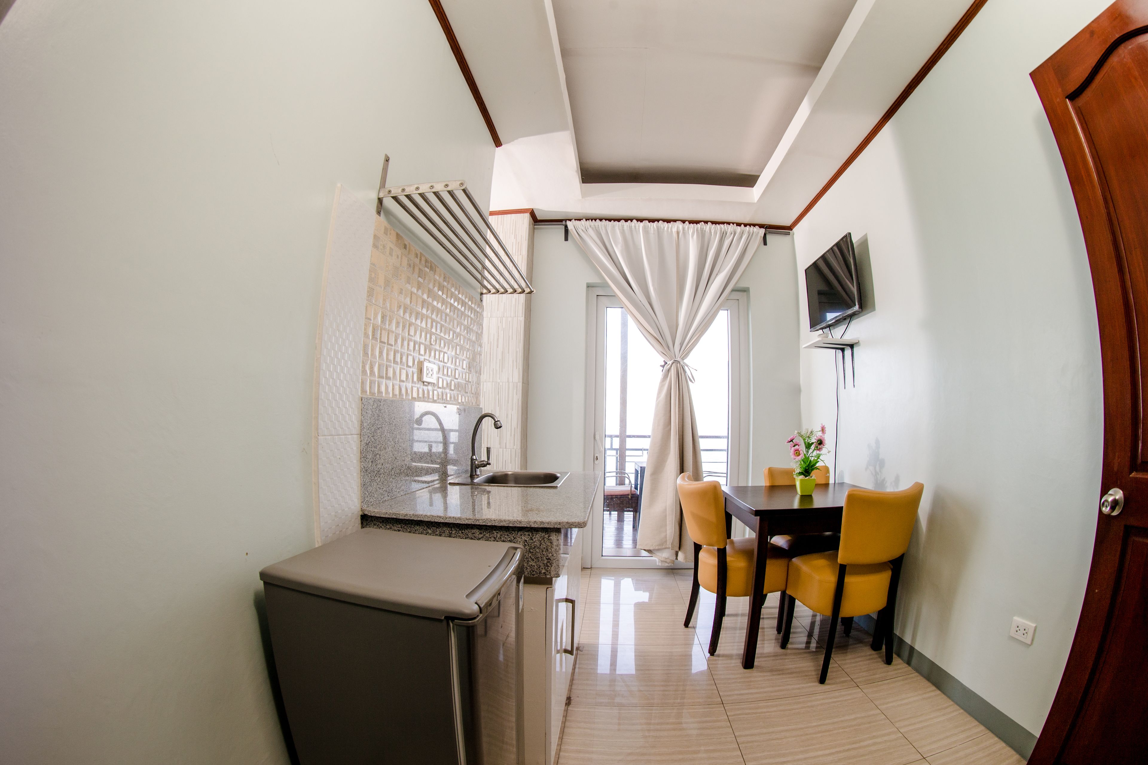 A compact kitchen with a refrigerator, sink, and a dining area with yellow chairs and a table.