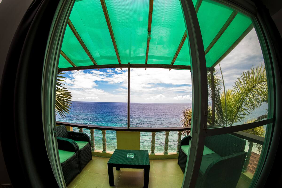 A room with a view of the ocean, a small table, and two wicker chairs.