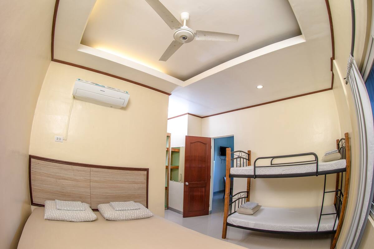 A room with a bunk bed, a ceiling fan, an air conditioning unit, and a door leading to another room.
