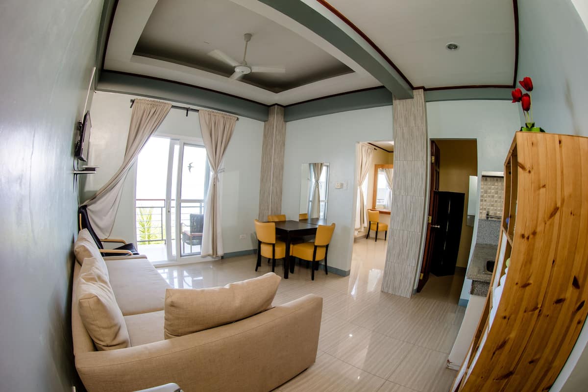 A spacious living area with a sofa, dining table, and chairs, a ceiling fan, and a view to the outside.