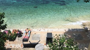 A beach view with clear water, a lounge area with chairs and a table, and a person sunbathing. - Seafari Resort Oslob (Oslob)