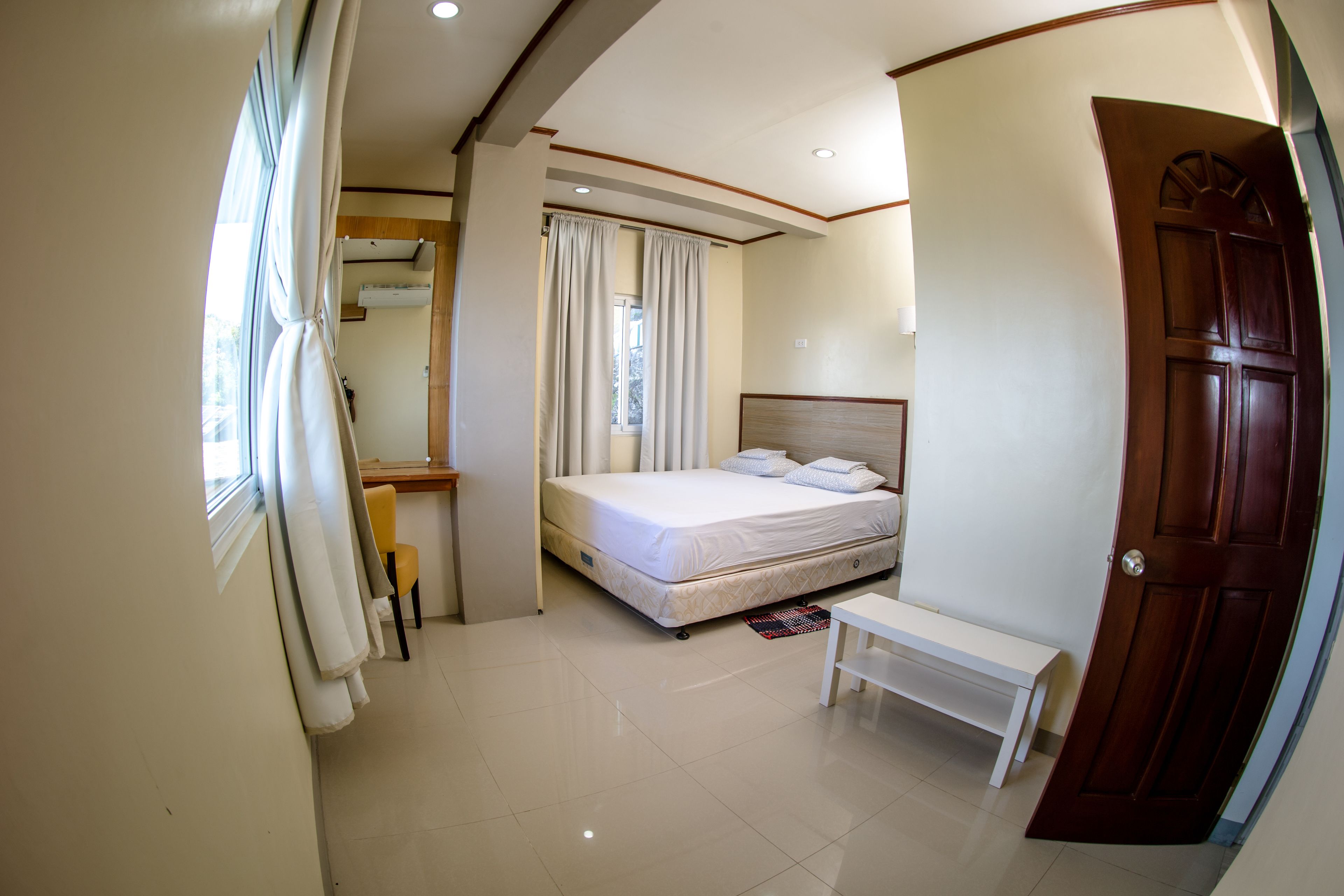A bedroom with a bed, a bench, a window with curtains, and a door.