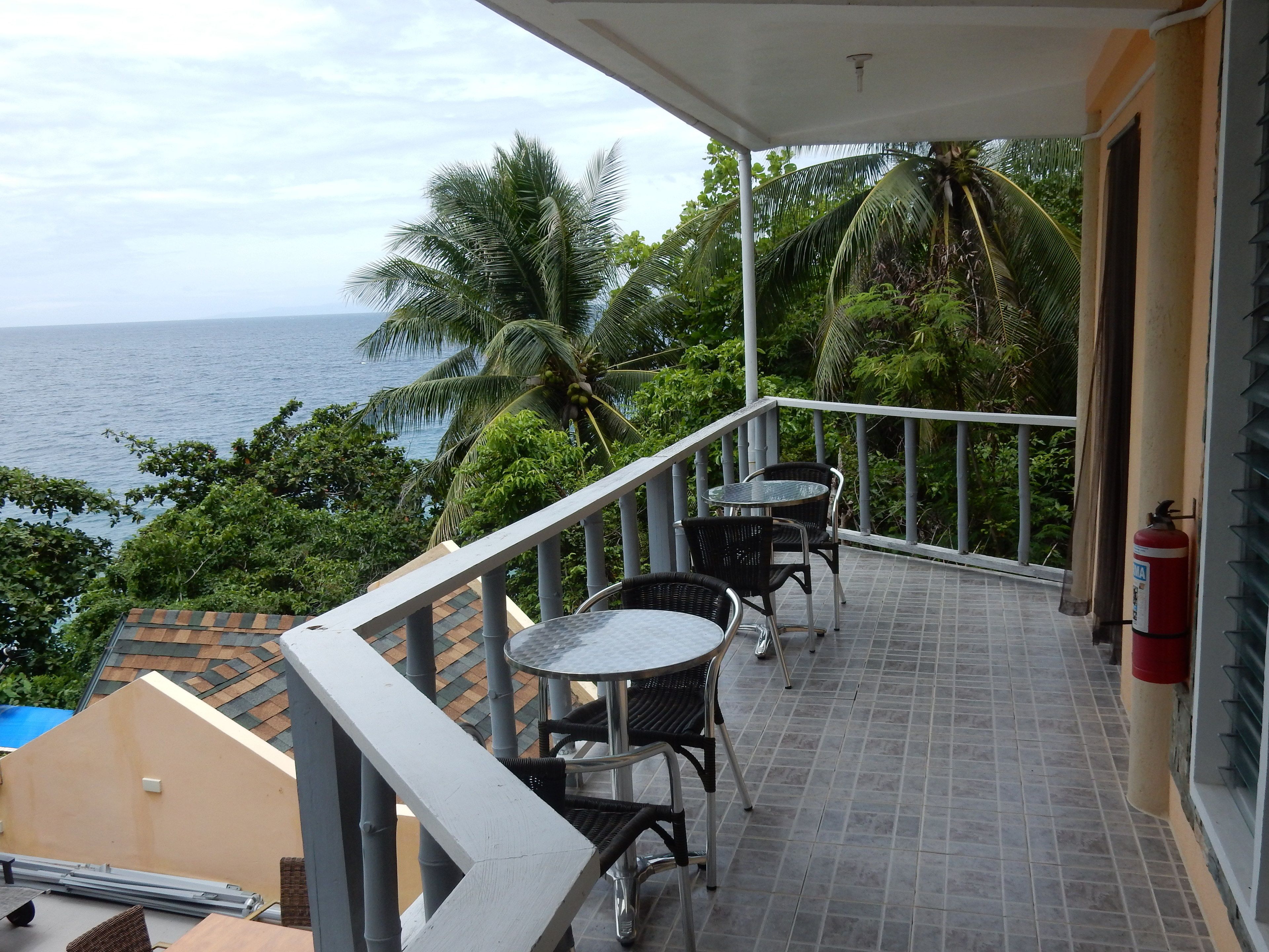 A balcony with a view of the sea, equipped with a table and chairs, and a fire extinguisher.
