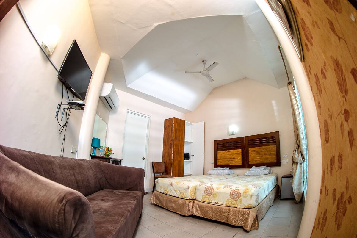 A bedroom with a bed, a sofa, a ceiling fan, and a TV mounted on the wall.