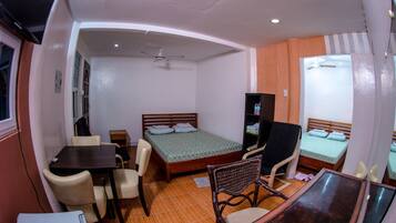 Habitación de hotel pequeña con una cama individual, un escritorio, una silla, un televisor y un armario.