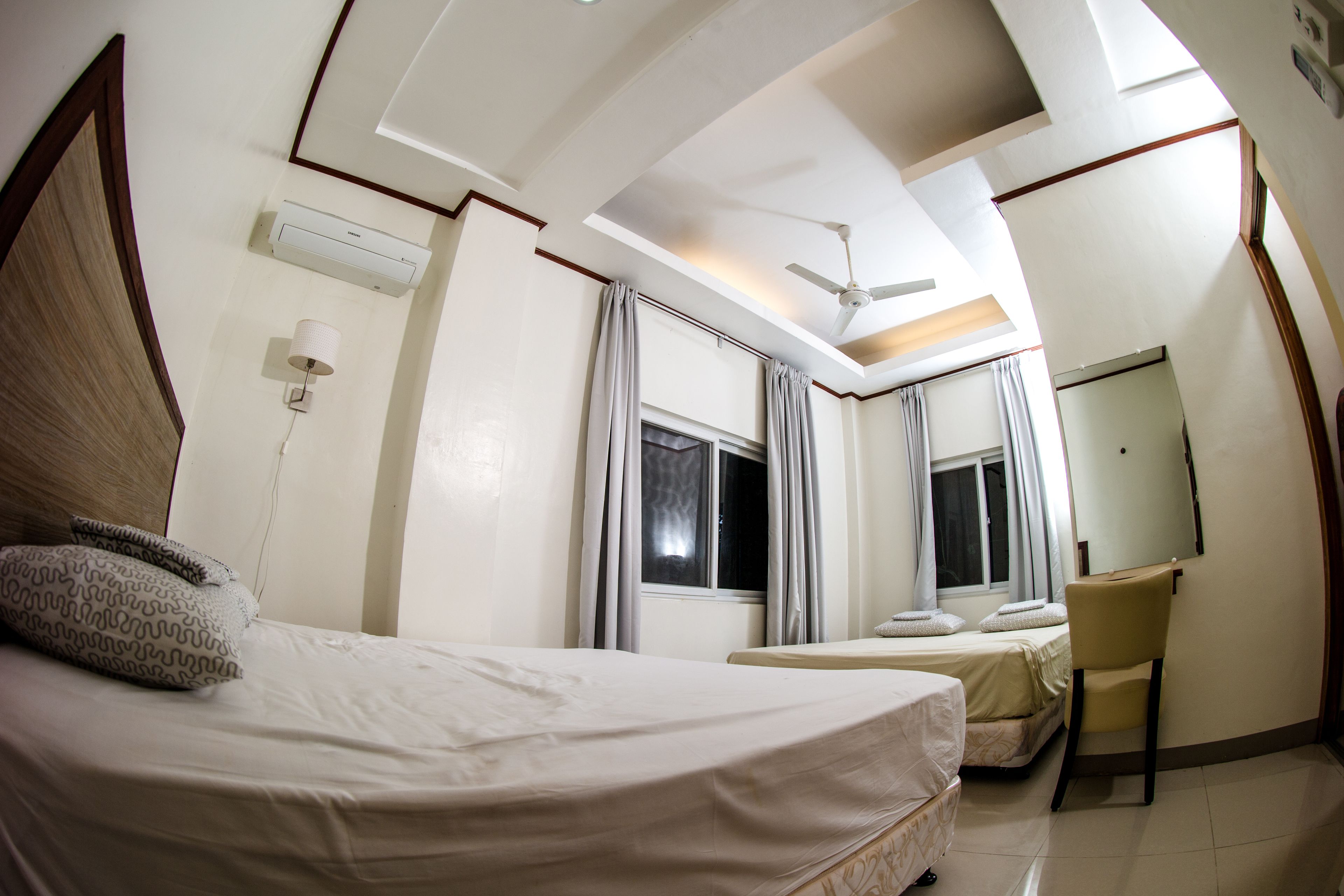 A hotel room with a bed, a desk, a chair, a ceiling fan, and a window with curtains.