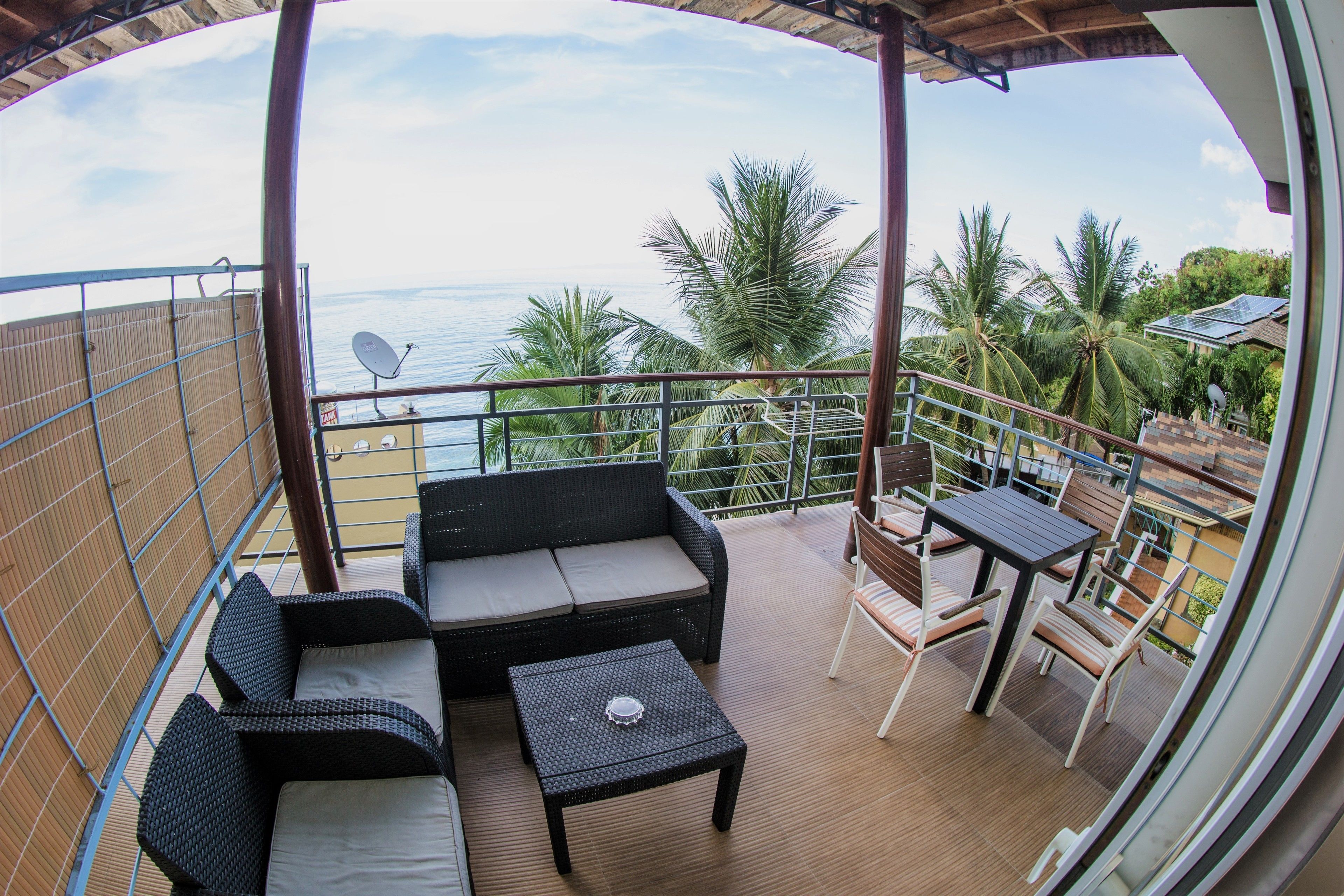 A balcony with wicker furniture, a table, and a view of the ocean and palm trees.