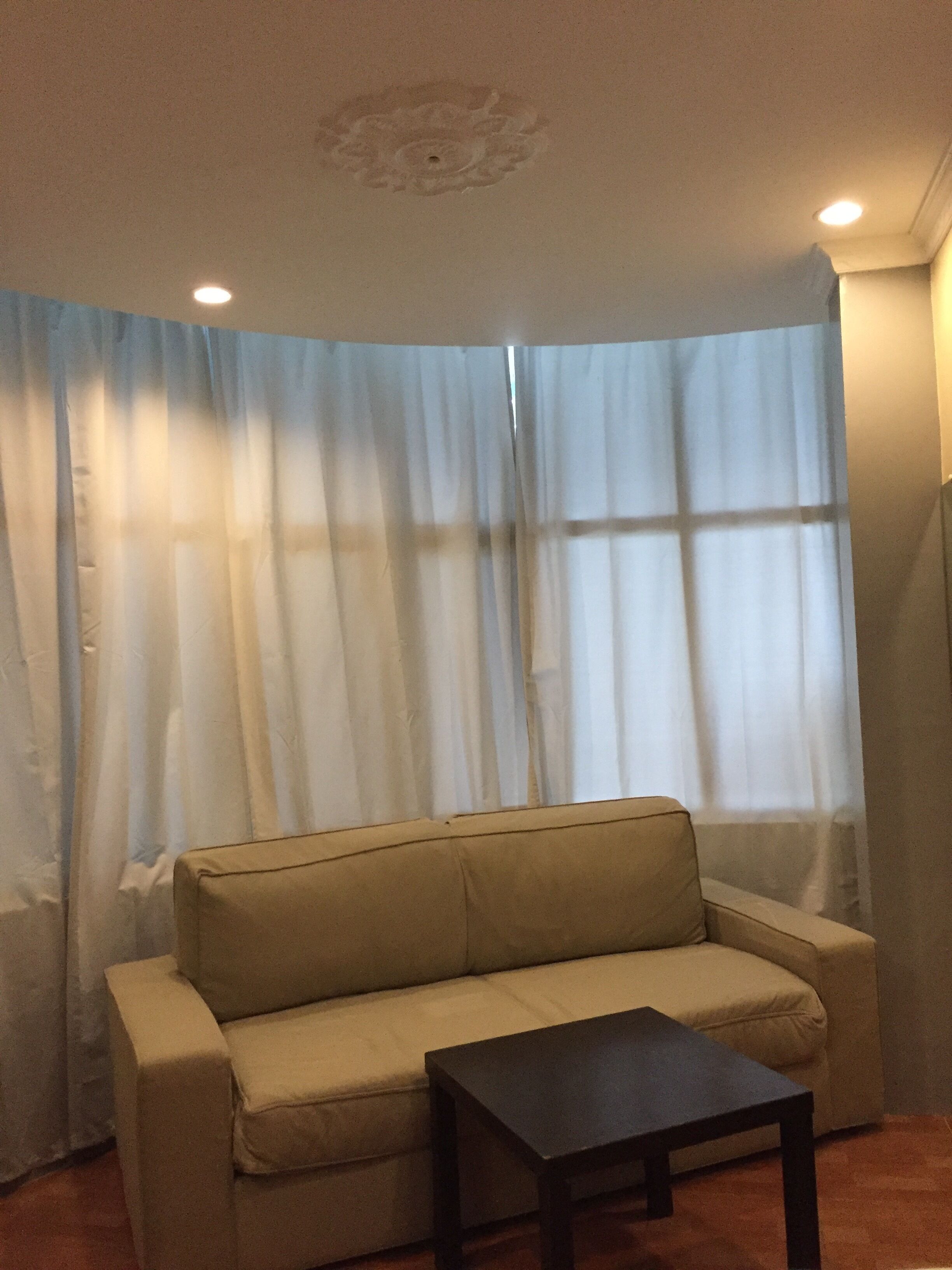 A living room with a beige sofa, a small black table, and a large window with sheer curtains.
