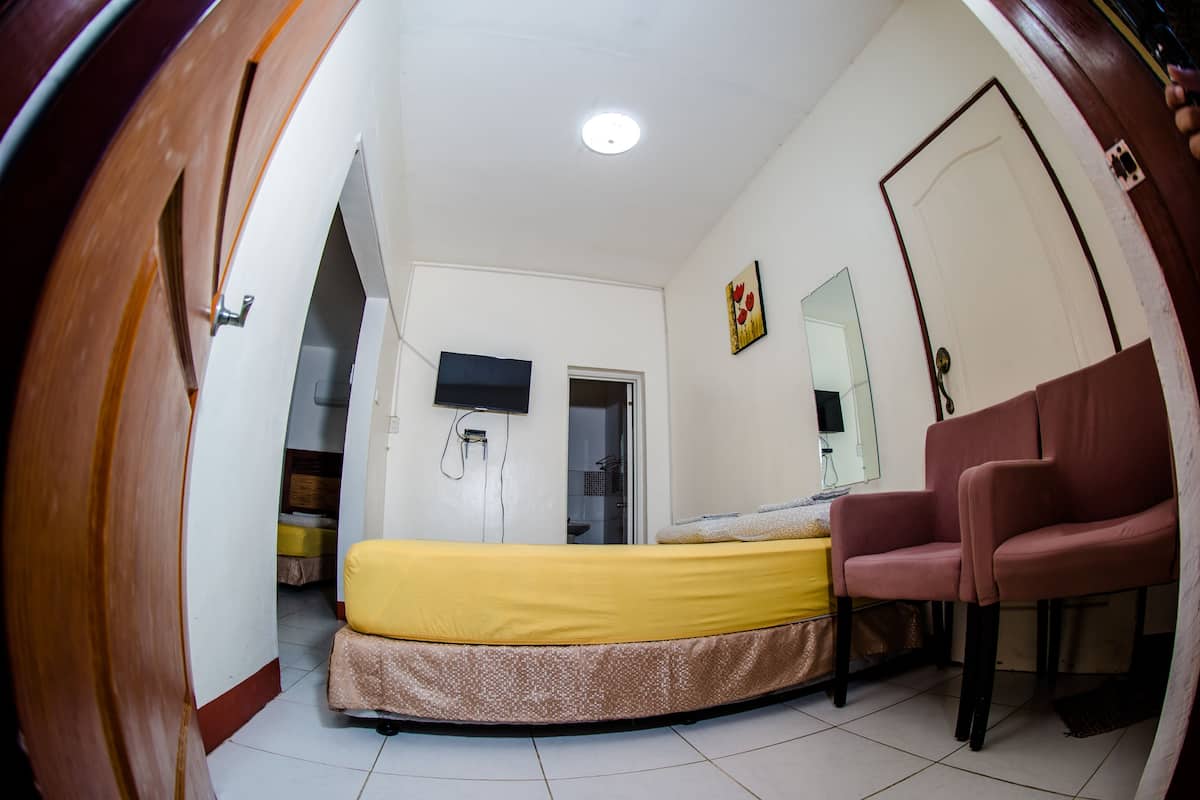 A compact room with a bed, a chair, a door, and a television on the wall.