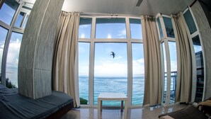 A room with a large window overlooking the sea, a bed, a small table, and a chair. - Seafari Resort Oslob (Oslob)