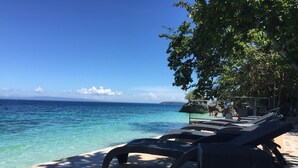 A beachside lounge area with lounge chairs and a netted area for swimming. - Seafari Resort Oslob (Oslob)