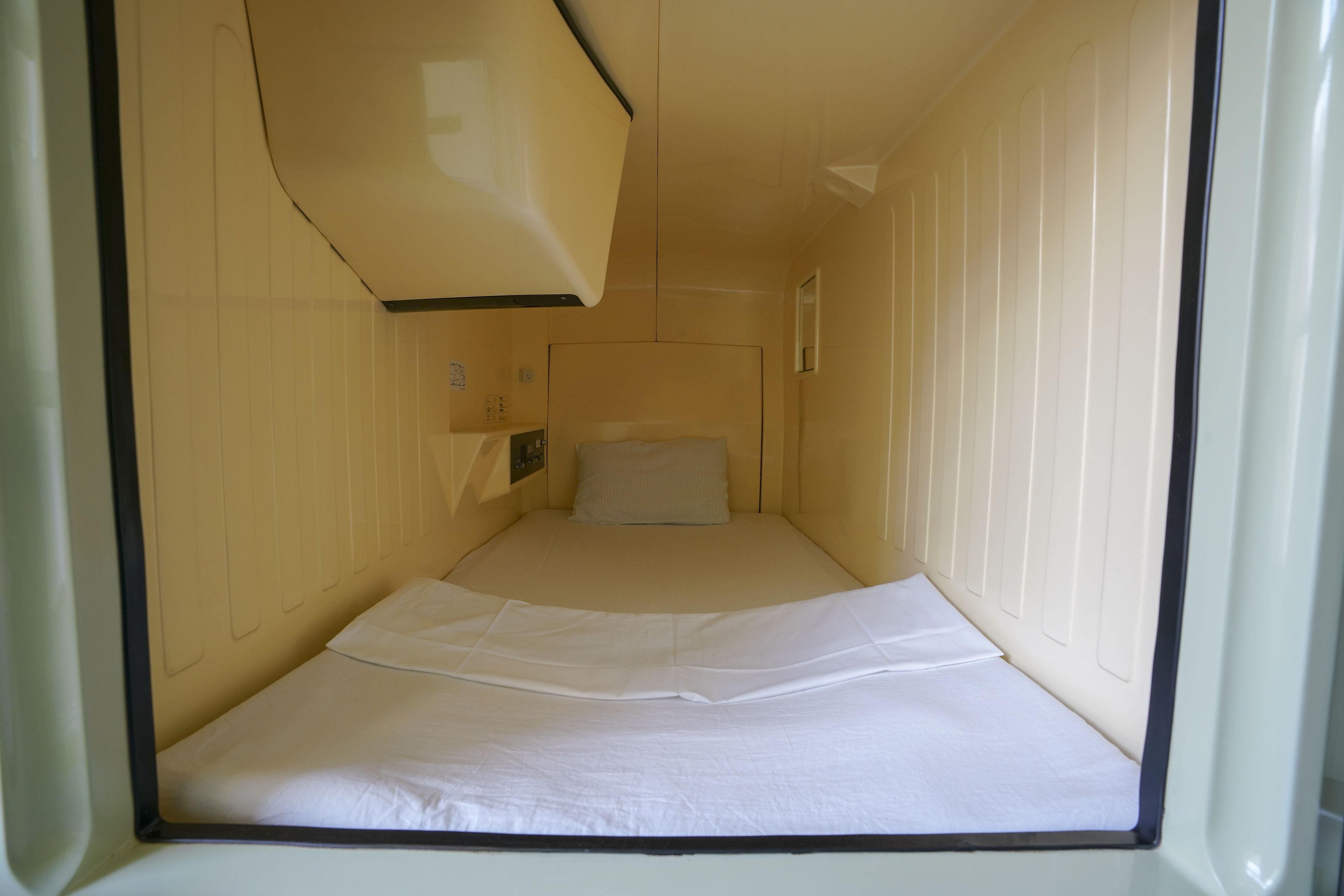 Une petite chambre avec un lit simple, disposant d’un aménagement simple, comprenant un lit, une petite table de chevet et un luminaire fixé au mur.