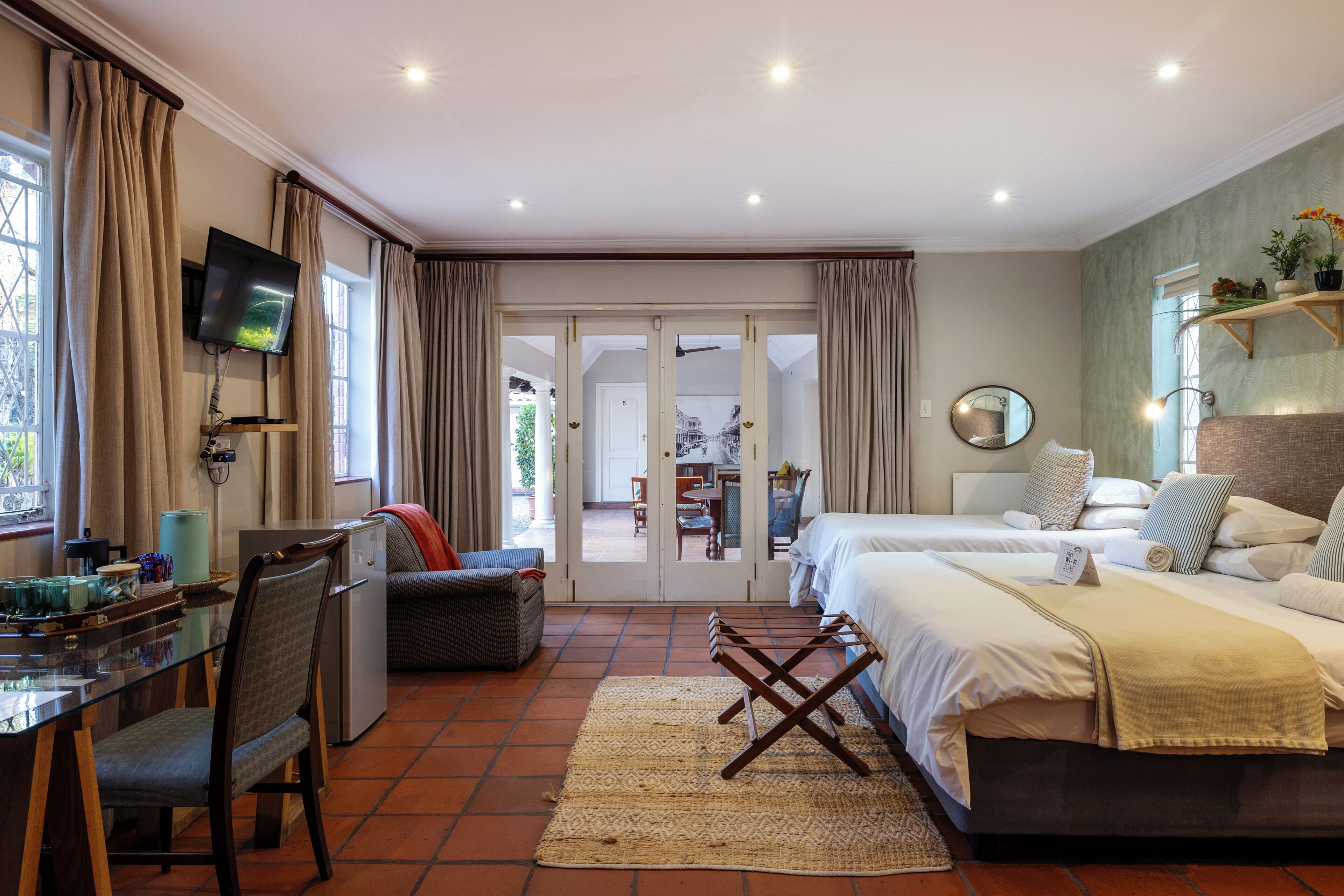 A hotel room with a TV, a desk with a chair, a bed, and a view of the outside.