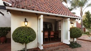Een huis met pannendak, een witte gevel en een bakstenen entree. Twee potplanten en een klein terras met een tafel en stoelen.