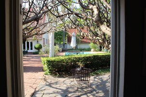 Un patio con una silla metálica y una mesa, un edificio blanco de techo rojo, y un seto al frente.
