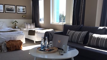 Una habitación de hotel con cama, sofá, una mesa de centro con bebidas y una computadora portátil, y una ventana con cortinas.