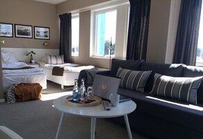 Una habitación de hotel moderna con una cama, un sofá, una mesa redonda con una computadora portátil y una ventana con cortinas.