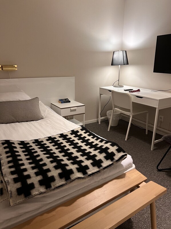 A hotel room with a bed, a desk, a chair, a lamp, and a TV.