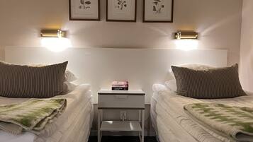 Una habitación de hotel con dos camas individuales, una mesita de noche pequeña y un estante fijado a la pared con impresiones botánicas enmarcadas.