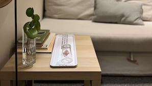 Une pièce avec une table en bois, un vase en verre contenant une plante, un tableau encadré et un canapé avec des coussins.
