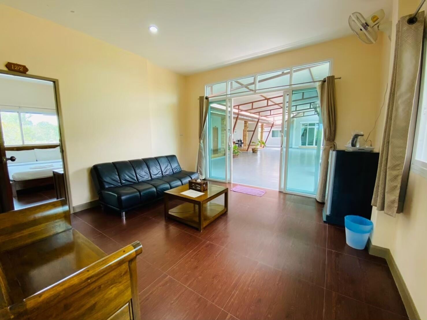Una sala de estar con un sofá de cuero negro, una mesa de centro de madera y un ventanal que da a un balcón.