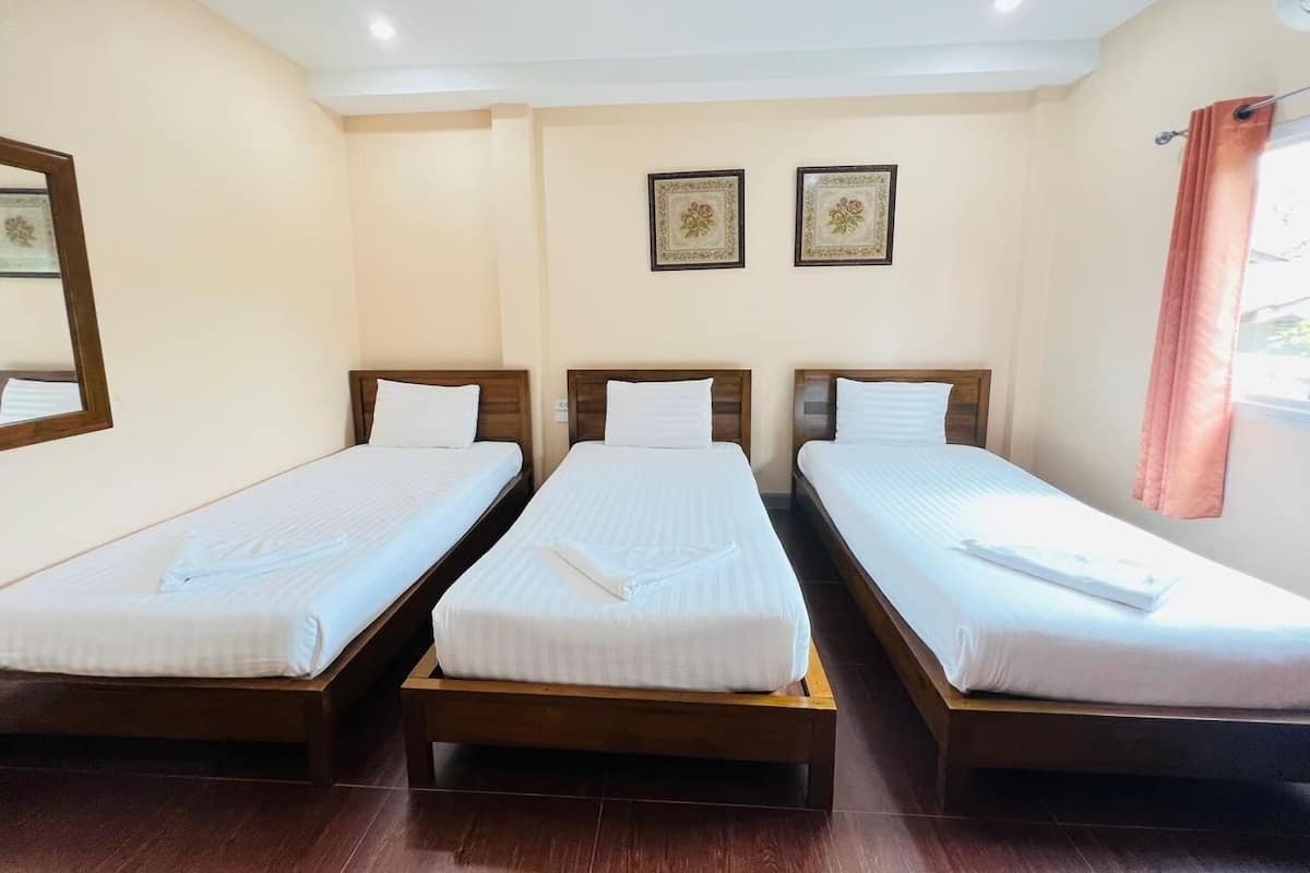 A hotel room with three single beds, a wooden floor, and a large mirror on the left wall.