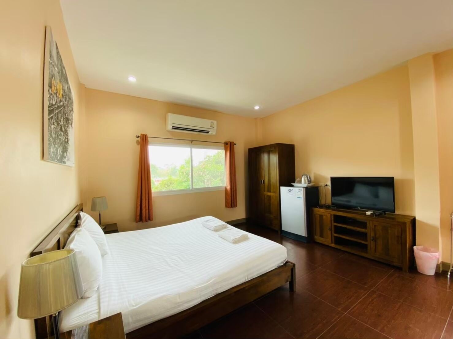 A hotel room with a bed, a TV, a wardrobe, and an air conditioning unit.