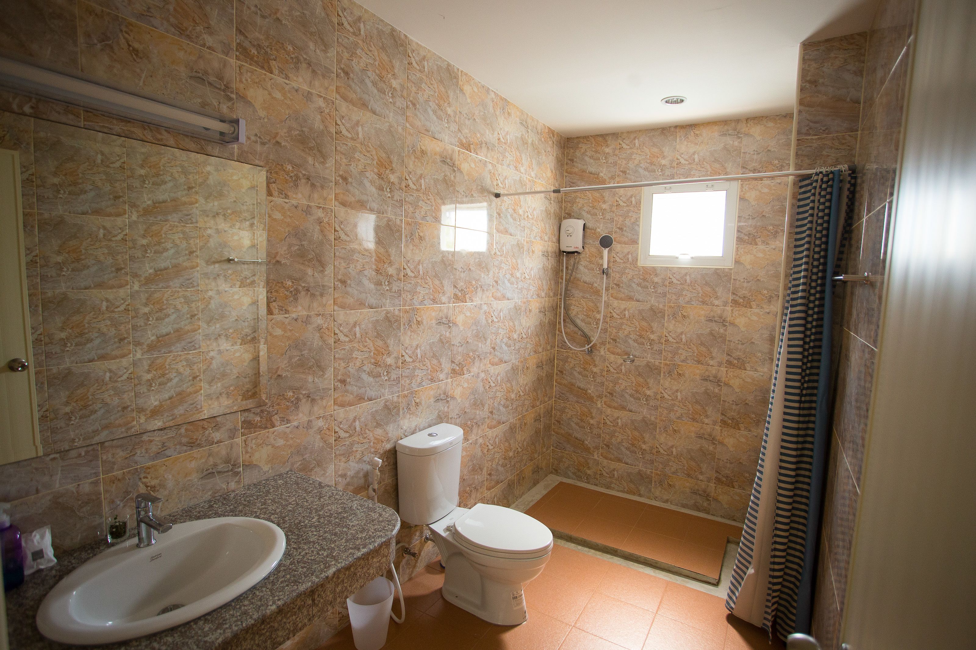Une salle de bain avec un mur en marbre, un lavabo, des toilettes, une douche et une fenêtre.
