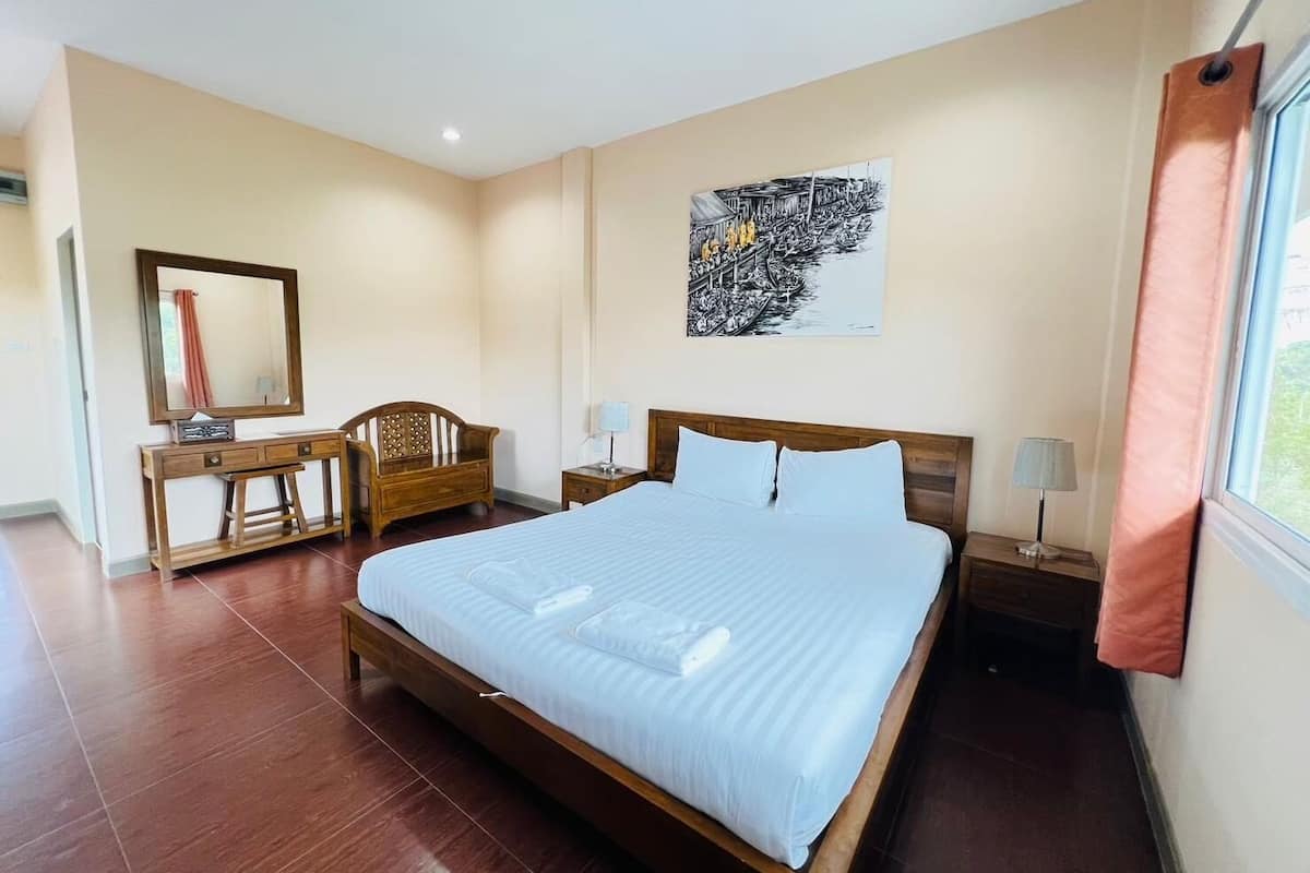 A bedroom with a large bed, a wooden desk, a chair, a nightstand, and a wall-mounted lamp.