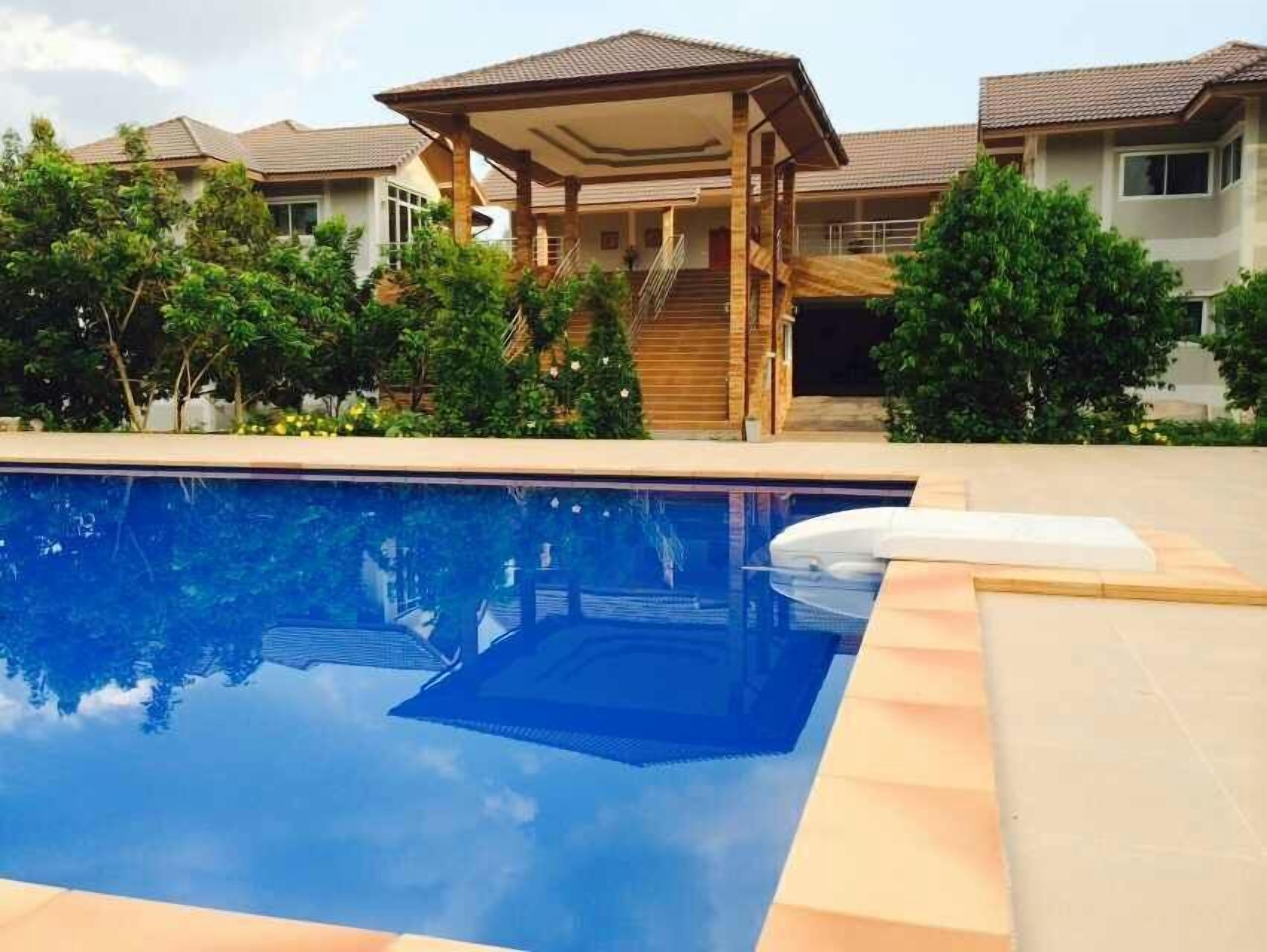 Una piscina con cubierta de madera y un área techada, rodeada de vegetación y edificios residenciales.