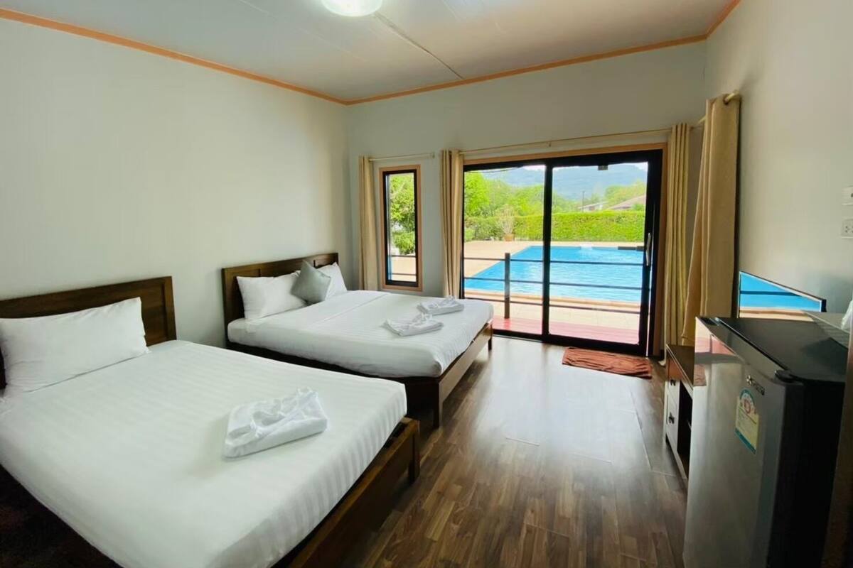A hotel room with two beds, a small kitchenette, and a sliding glass door leading to a pool.
