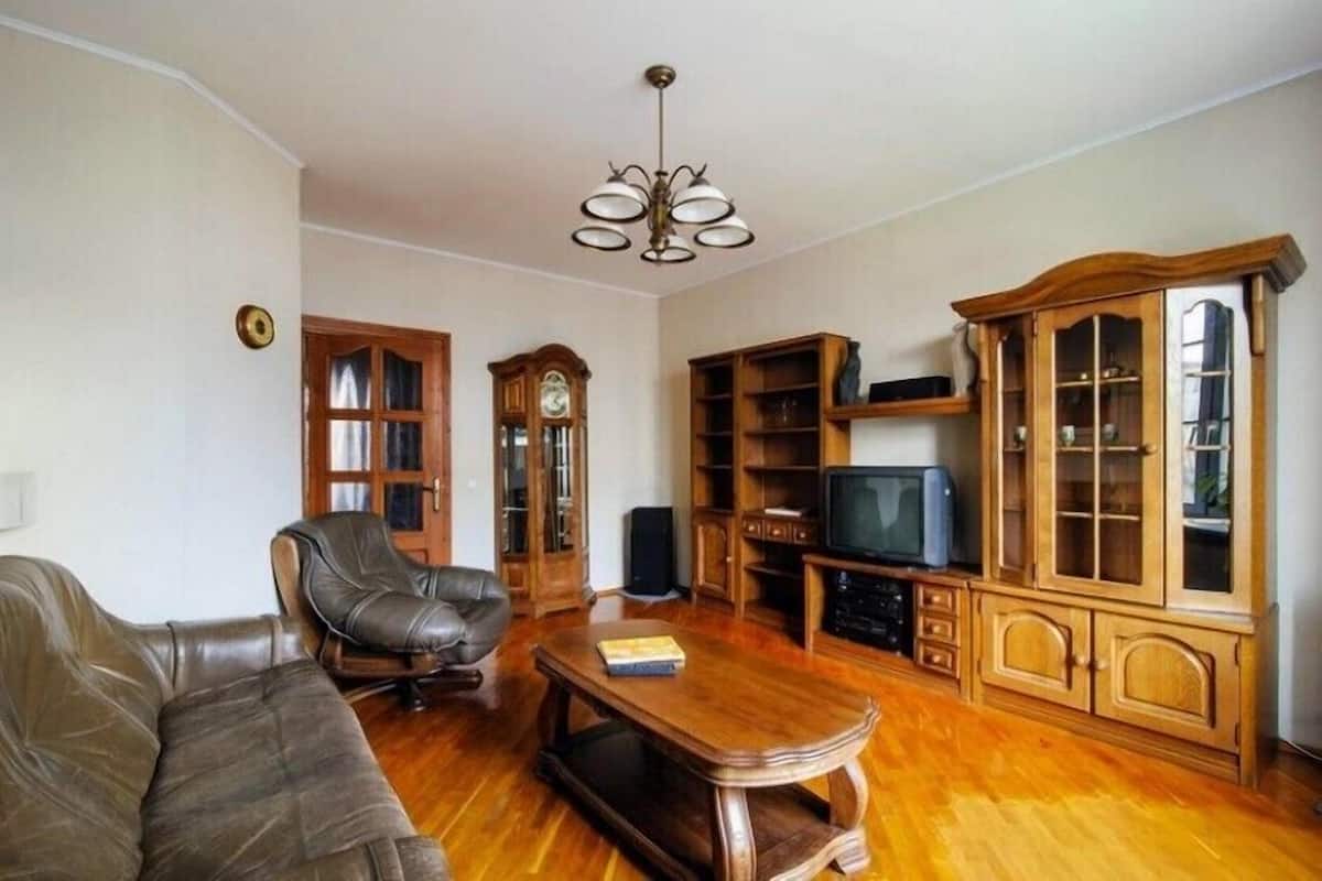 A living room with a leather sofa, wooden cabinet, television, and a ceiling fan.