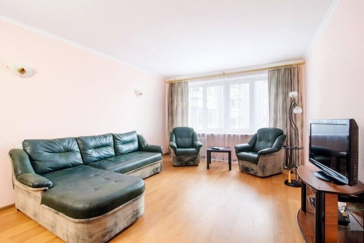 A living room with a green leather sofa, two armchairs, a small table, and a TV on a wooden stand.