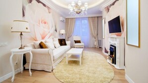 Uma sala de estar com um sofá branco, uma mesa de centro, um candelabro, uma lareira e um grande quadro de rosas na parede.