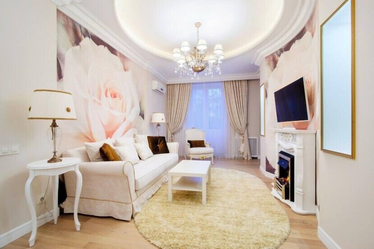 A living room with a white sofa, a coffee table, a chandelier, a fireplace, and a large rose painting on the wall.