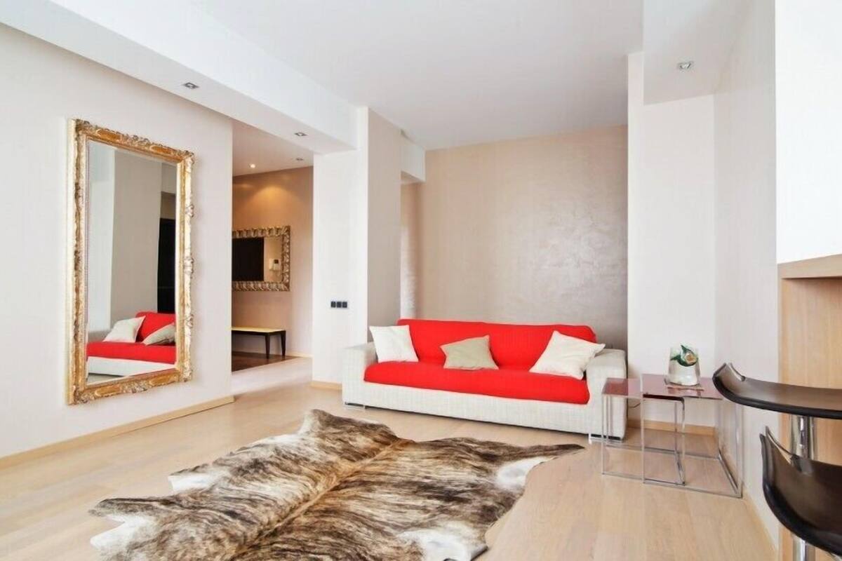 A modern living room with a white sofa, a red throw, a large mirror, and a fur rug.