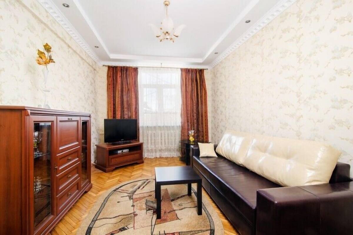 A living room with a sofa, TV, wooden cabinet, and a patterned rug.