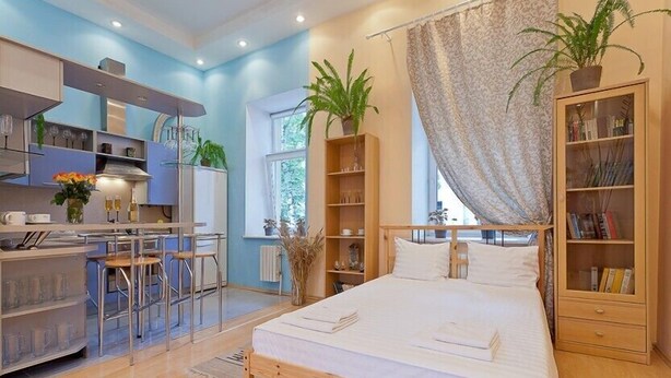 Quarto moderno com cama, mesas de cabeceira, guarda-roupa e área de cozinha com banquetas.
