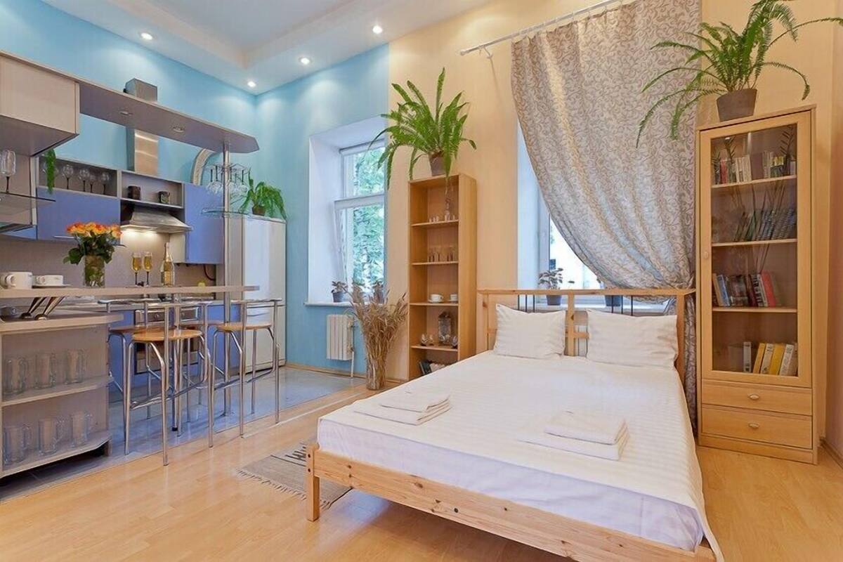 A modern bedroom with a bed, bedside tables, a wardrobe, and a kitchen area with bar stools.
