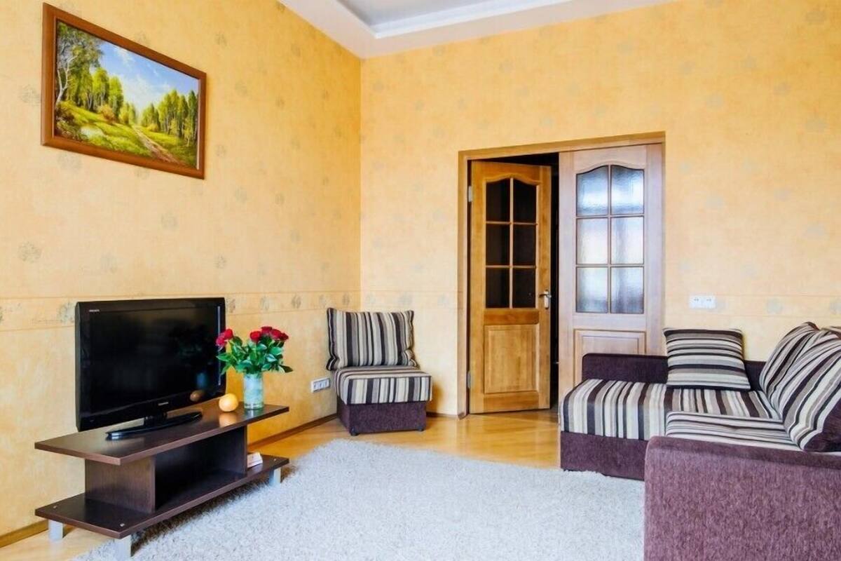 A living room with a TV, two sofas, a striped armchair, and a painting on the wall.