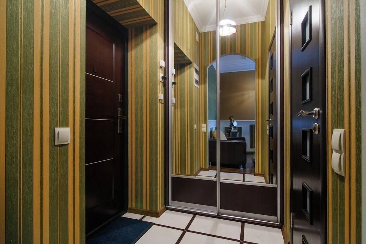 A hotel hallway with striped walls, a dark wooden door, and a glass door leading to a bathroom.