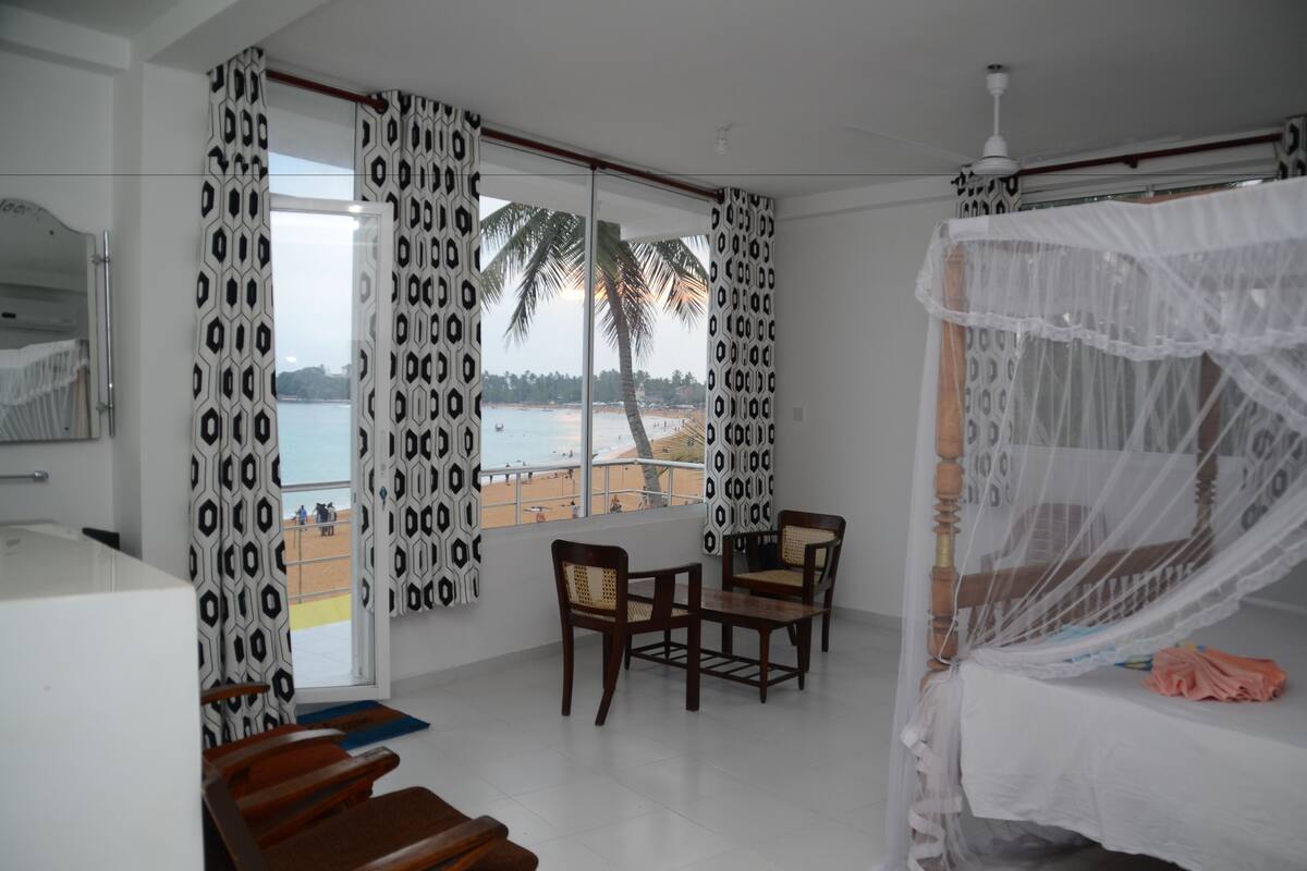 Un dormitorio con cama, una mesa, dos sillas y vista a la playa.